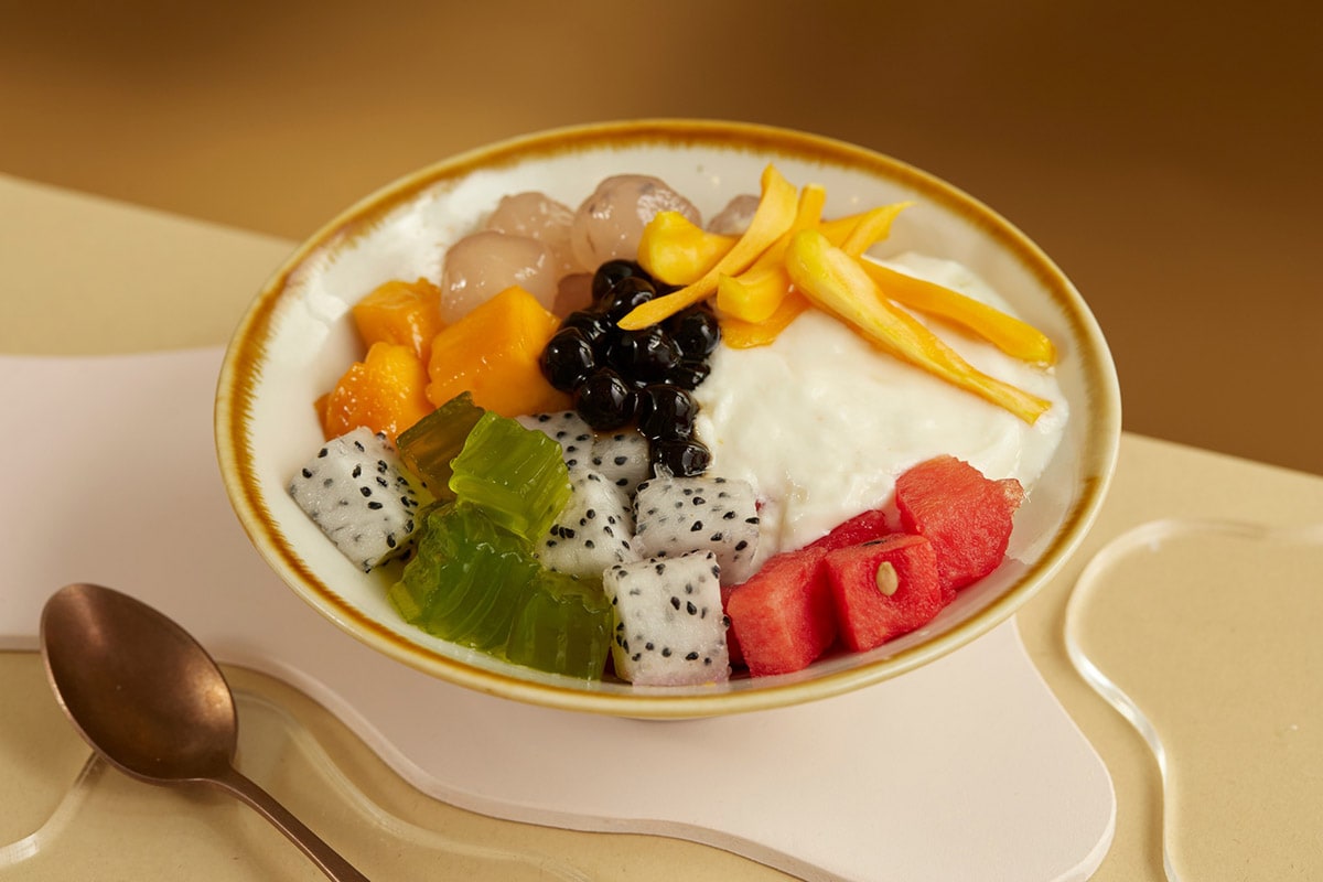 A rainbow bowl of hoa qua dam featuring colorful fruit pieces - pink dragon fruit, red watermelon, yellow mango, white longan, with crushed ice 